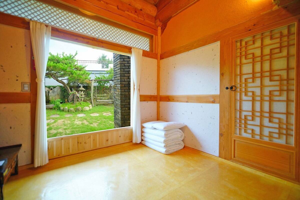 A traditional Japanese room with tatami flooring, a sliding door with a geometric pattern, and a view of a garden with a stone lantern.
