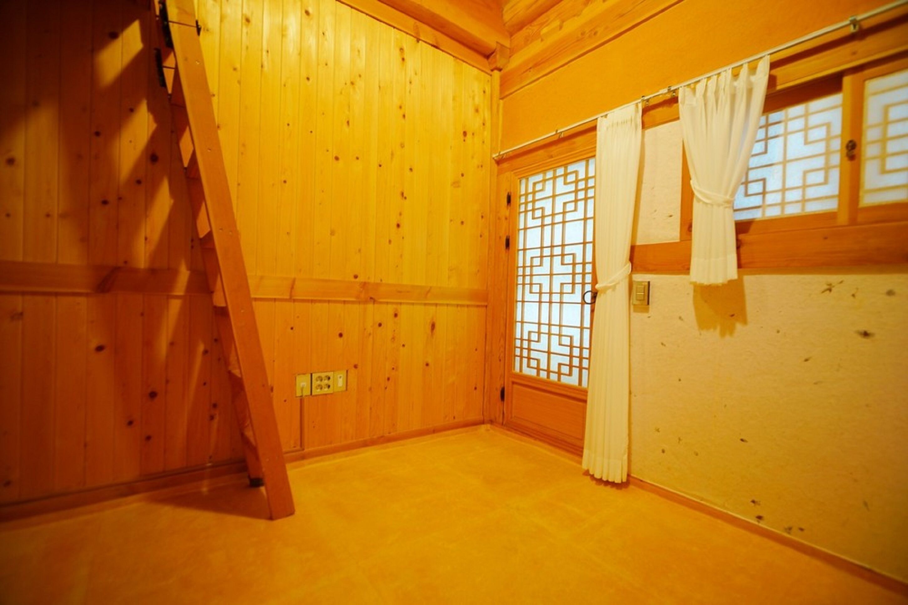 Una habitación con paredes de madera, una puerta corredera con un diseño geométrico y una escalera apoyada en la pared.