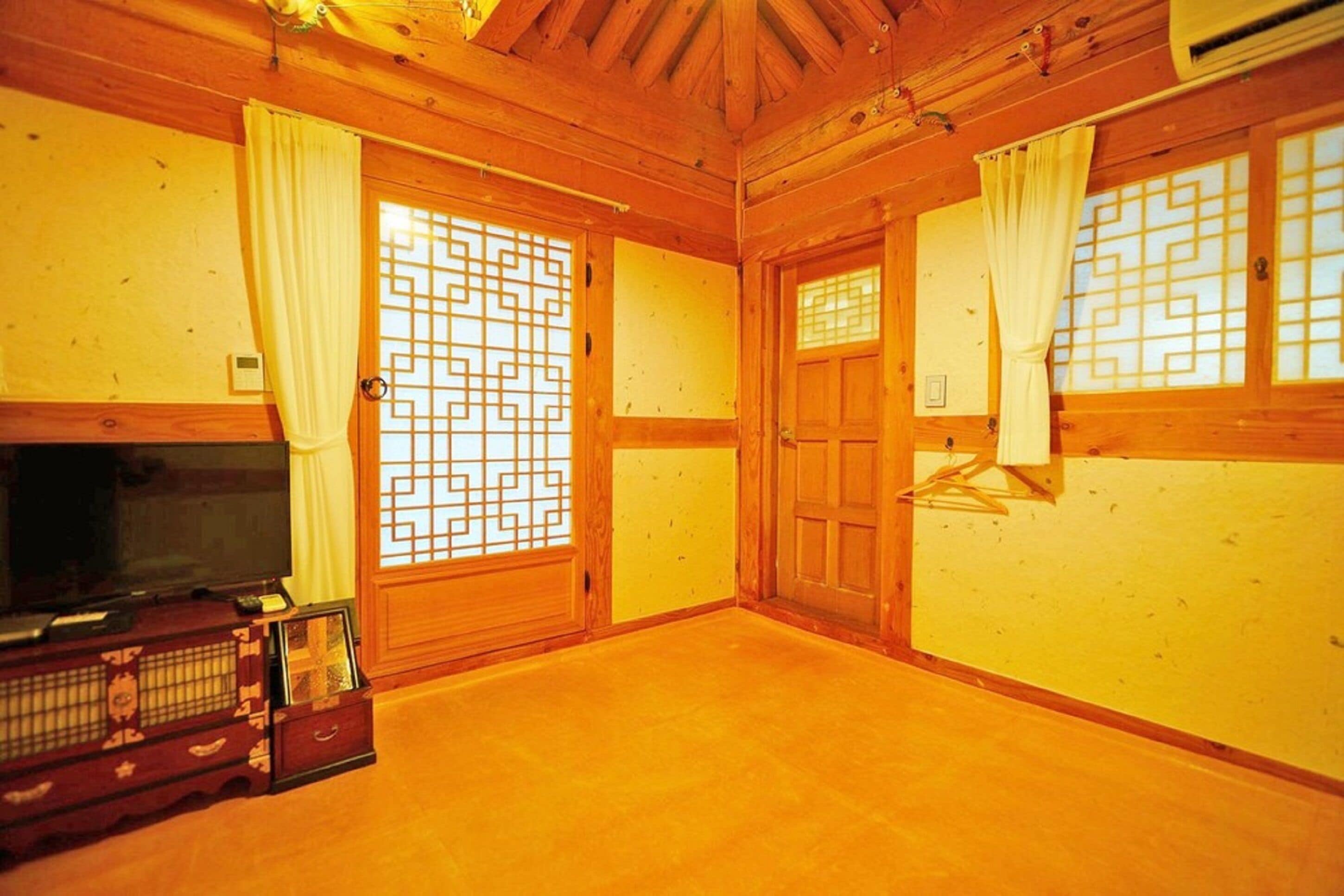 A traditional Japanese room with tatami flooring, sliding doors with geometric patterns, a television on a low wooden stand, and a small cabinet with a decorative top.
