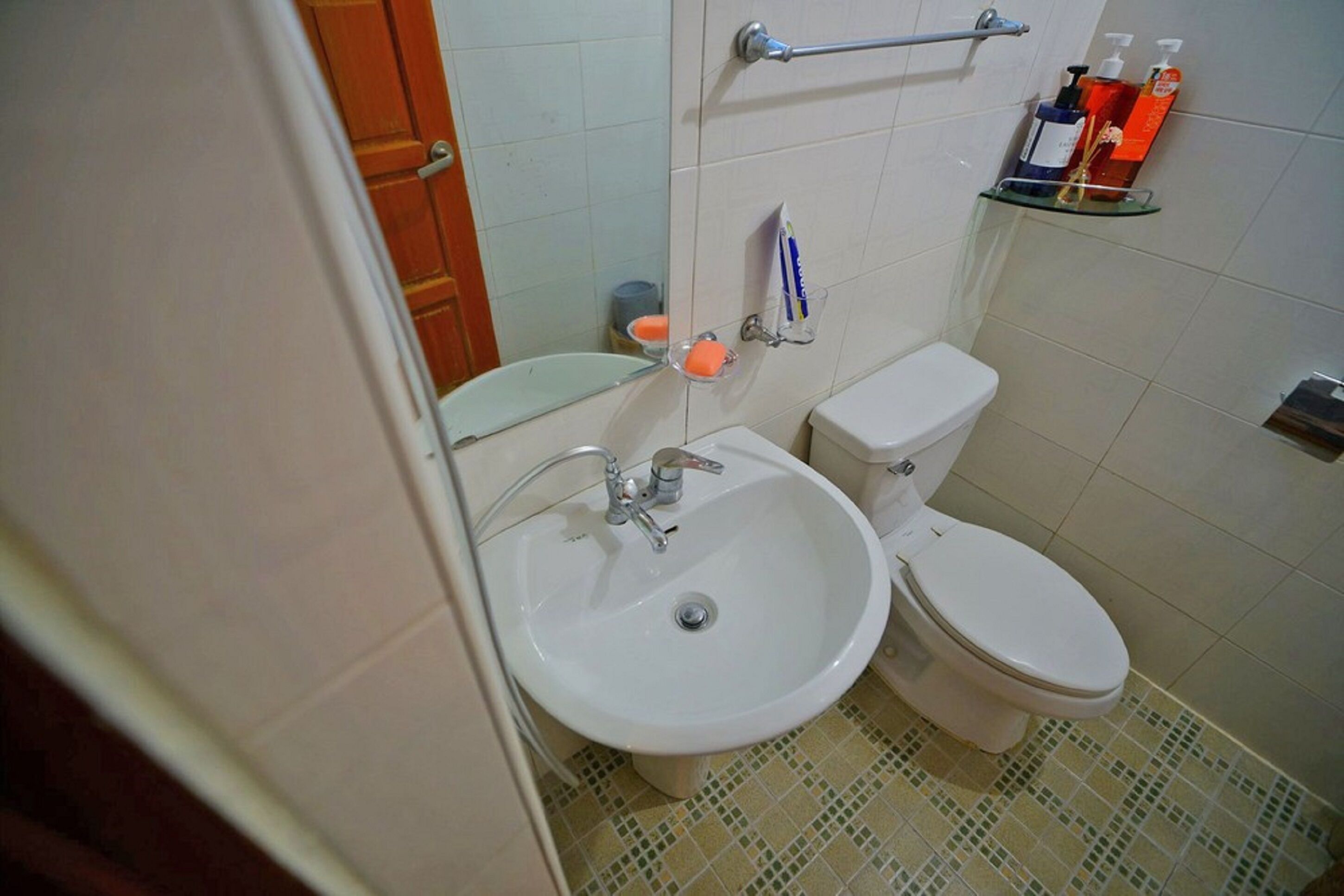 Une salle de bain avec un lavabo blanc, des toilettes et une étagère en verre où sont rangés les articles de toilette.