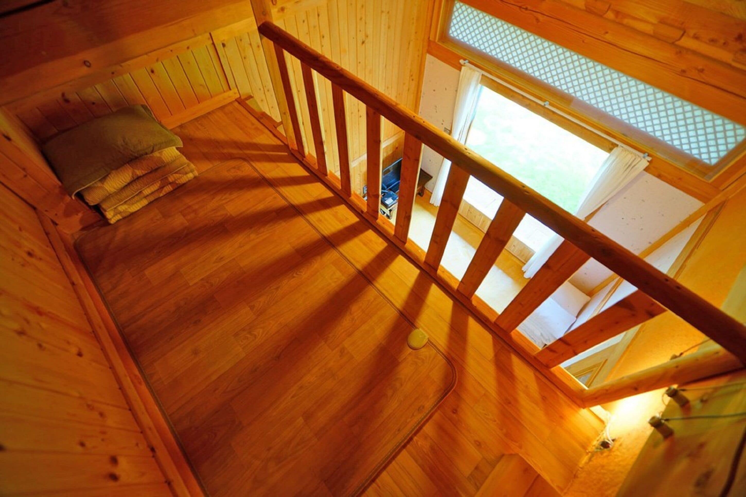 A wooden interior with a staircase, a bed with pillows, and a window with a view.