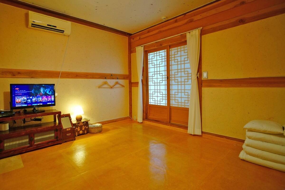 A living room with a wooden floor, a television, a traditional Japanese sliding door, and a small table with a lamp.
