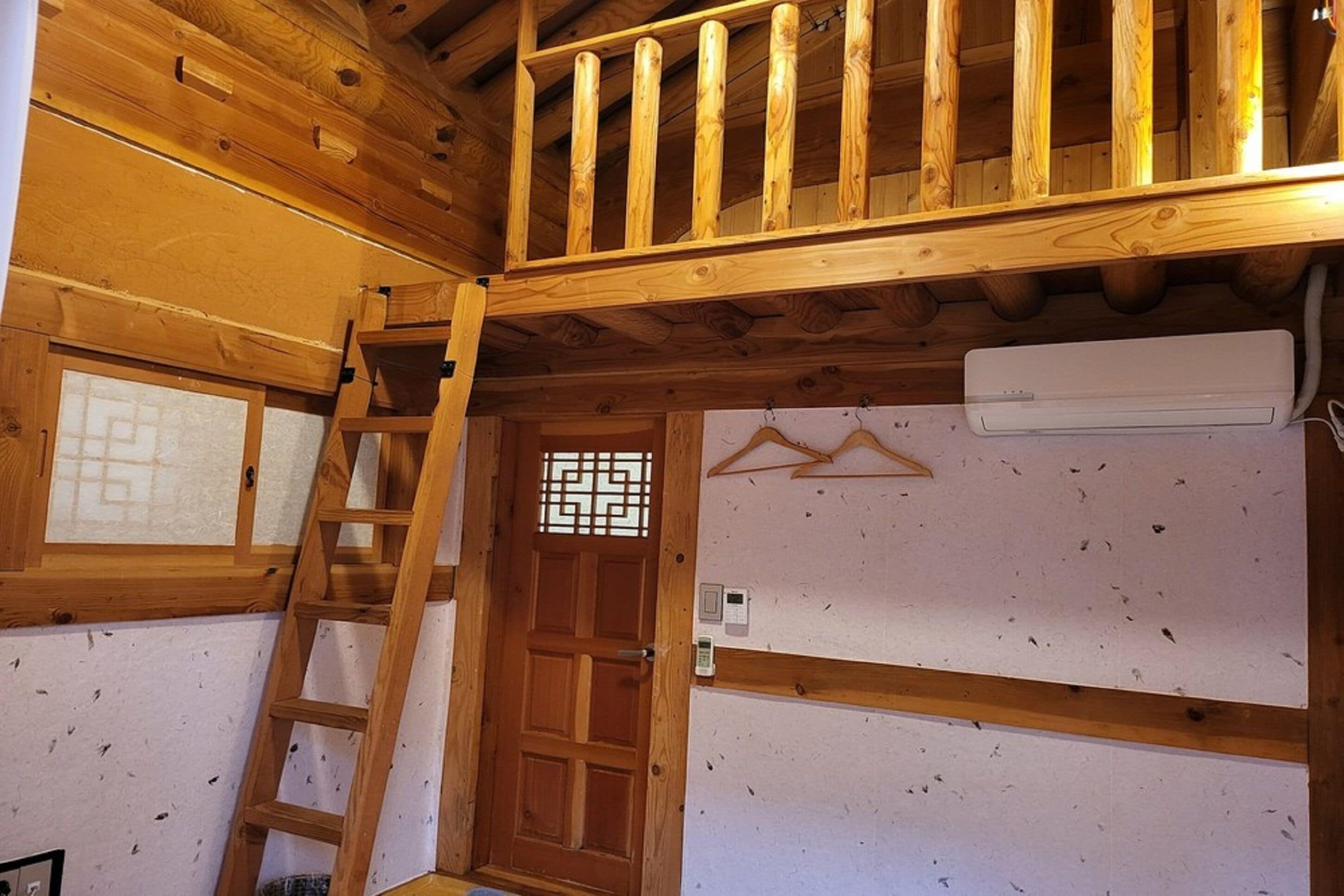 A room with a wooden ceiling, a wooden door with a decorative glass panel, a white air conditioning unit, and a wooden ladder.