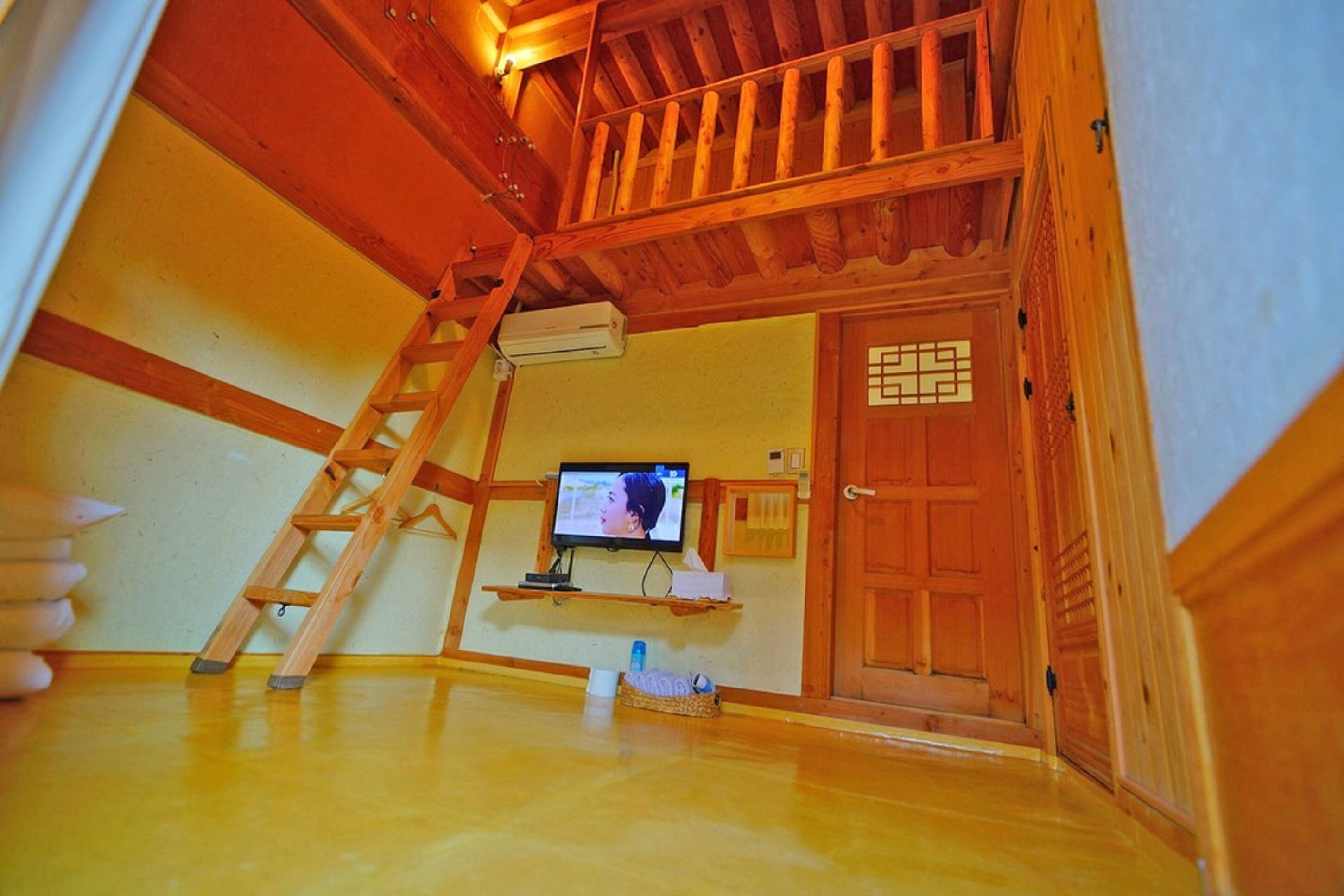 A wooden interior with a television on a shelf, a ladder, and a door with a decorative panel.