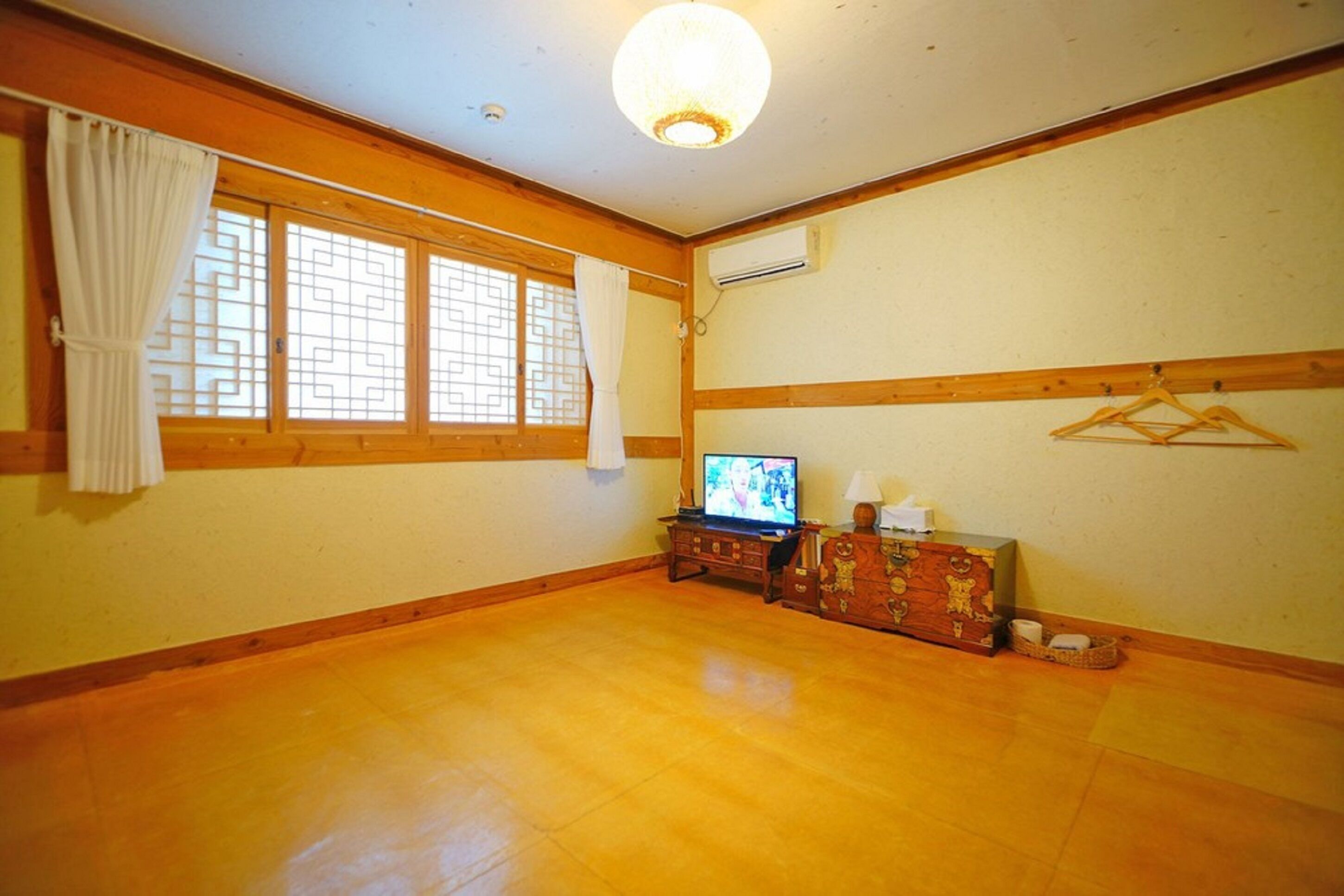 A room with wooden flooring, a television, a dresser, and a hanging clothes rack.