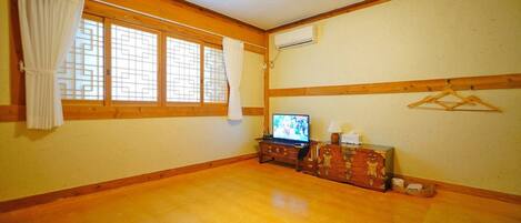 A room with wooden flooring, a television, a dresser, and a hanging clothes rack.