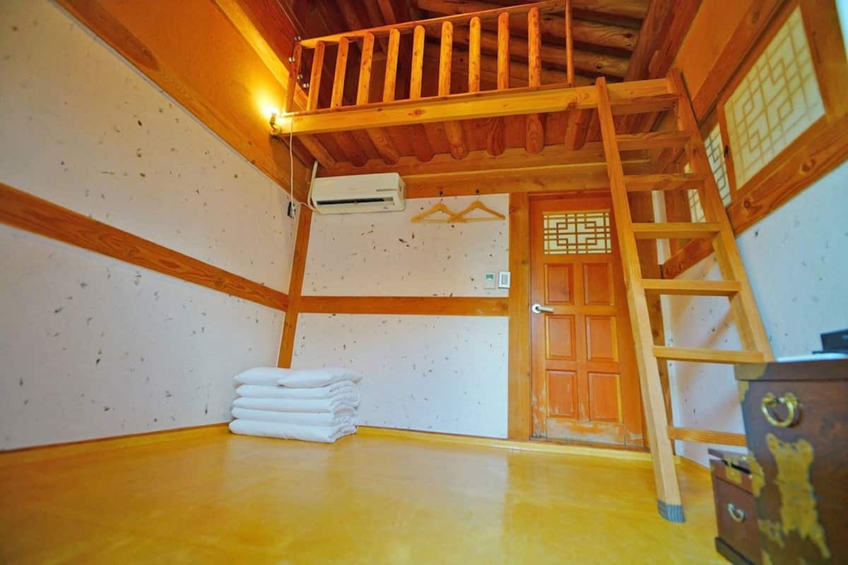 A room with a wooden ceiling, a wooden door, a ladder, and a stack of white towels.