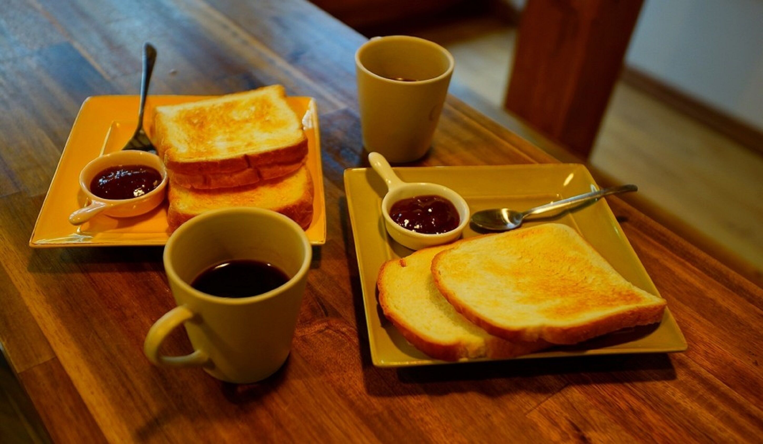 A table with two plates of toast, each with a small bowl of jam and a cup of coffee.