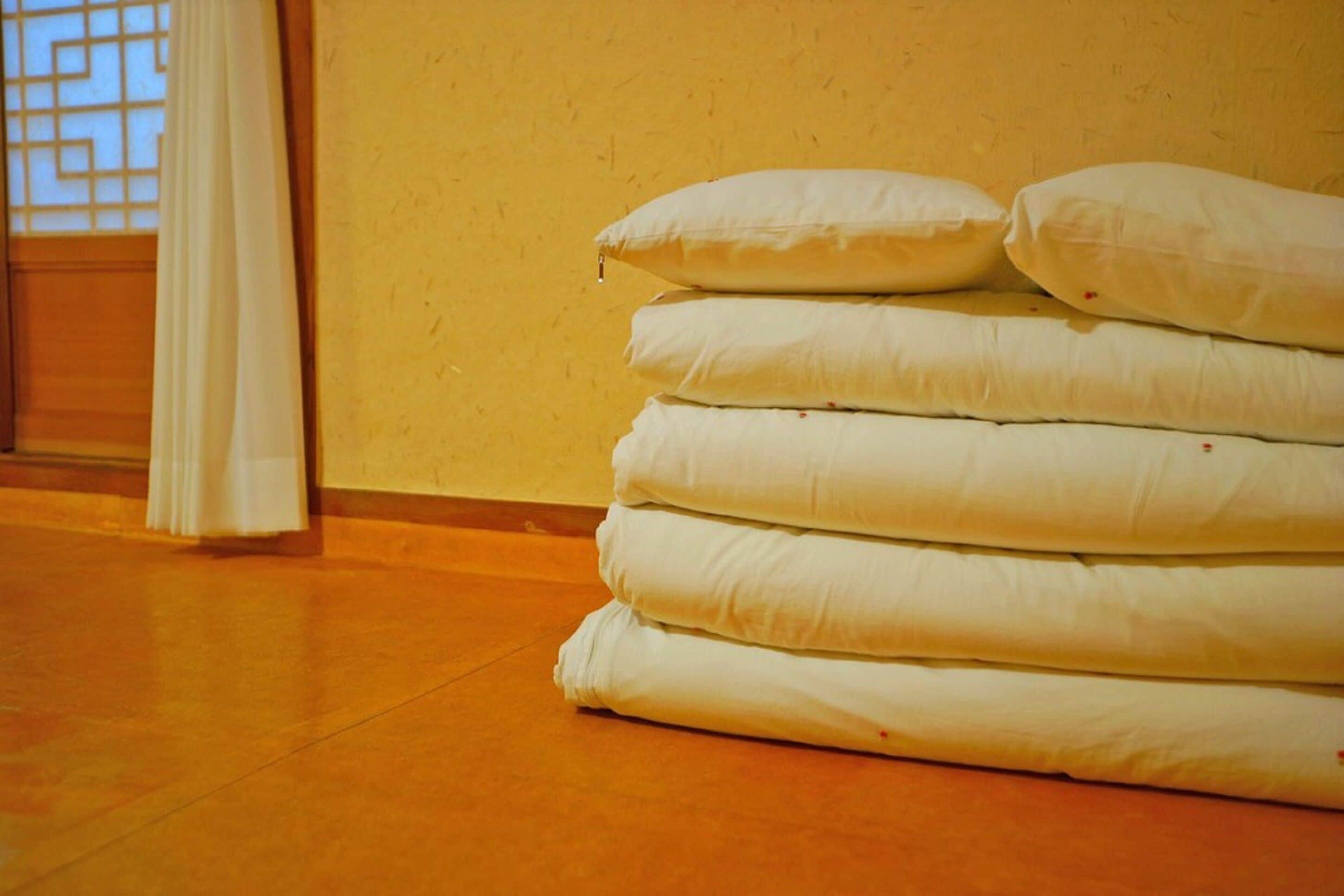 Un montón de almohadas blancas contra una pared amarilla en una habitación con suelo de madera.