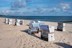 Genummerde strandstoelen, opgesteld aan een zandstrand in de buurt van het water.