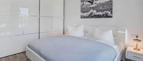 A modern bedroom with a large bed, a bedside table with a lamp, a wall-mounted artwork, and a large wardrobe.