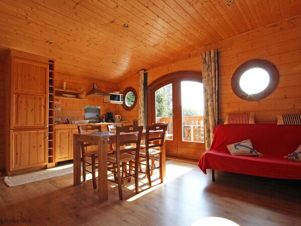 A wooden cabin with a dining area, kitchen, and a red sofa.
