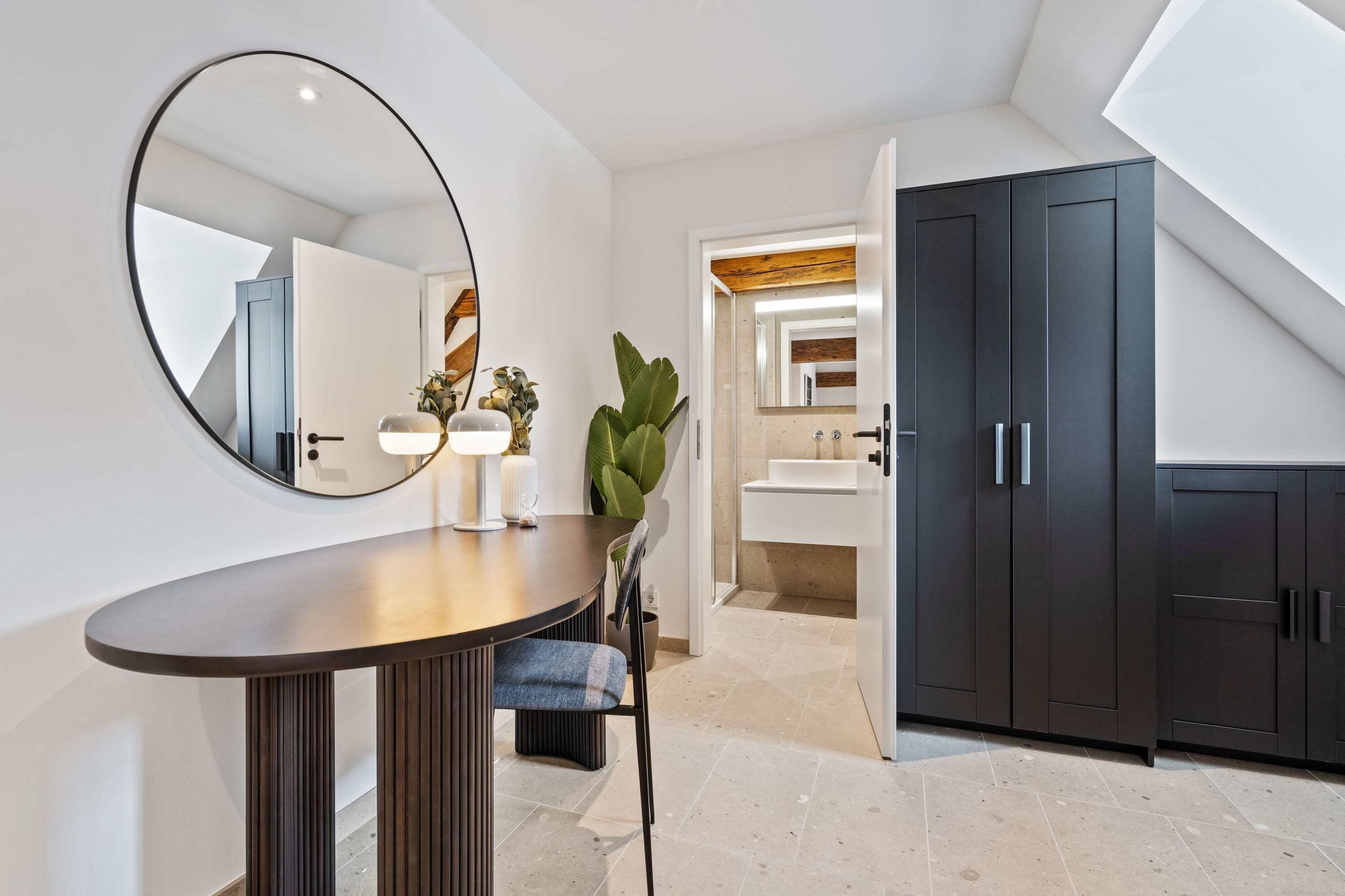 Une salle de bain moderne avec un grand miroir, une table ronde et des meubles sombres.