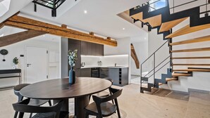 Eine moderne Küche mit einer zentralen Kochinsel, integrierten Geräten und einer Treppe mit Holzdielen und schwarzen Geländern.