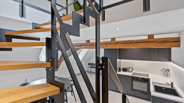 Eine moderne Küche mit Einbauofen und Spüle, ein Essbereich mit Tisch und Stühlen sowie eine Treppe mit Holz- und Metallelementen.