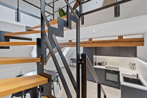 Una cocina moderna con horno empotrado y lavamanos, un comedor con mesa y sillas, y una escalera con elementos de madera y metal.