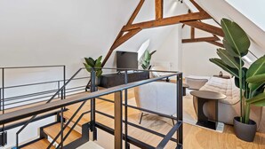 Ein modernes Loft mit freiliegenden Holzbalken, einer Treppe, einer Couch, einem Couchtisch und Topfpflanzen.