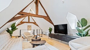 Ein modernes Wohnzimmer im Loft-Stil mit freiliegenden Holzbalken, einem Flachbildfernseher und bequemen Sitzgelegenheiten.