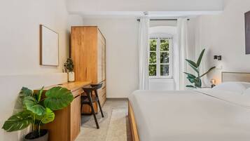 A bedroom with a bed, a desk, a chair, a potted plant, and a window with curtains.