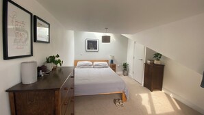 Een slaapkamer met een bed, een dressoir en twee ingelijste kunstwerken aan de muur.