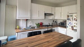 Een moderne keuken met witte kasten, een houten aanrecht, een gasfornuis, een spoelbak en een koelkast met magneetjes.