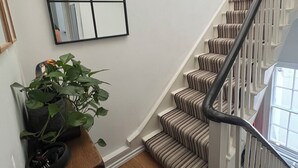 Een trap met gestreept tapijt, een houten bankje met een plant in pot, en een spiegel aan de muur.