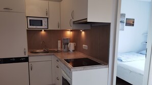 Een kleine keuken met een magnetron, koffiezetapparaat en oven. Een bed is zichtbaar in de aangrenzende kamer.