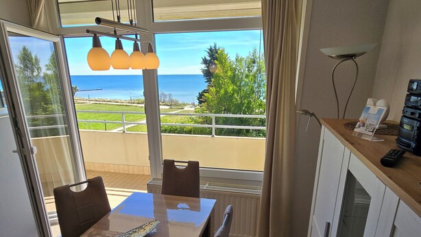 Een eetgedeelte met uitzicht op zee, een tafel met stoelen, een hanglamp en een keuken met apparatuur.