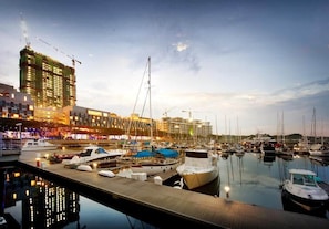 A marina with boats docked, a construction crane, and buildings in the background.