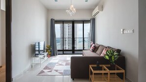 Ein modernes Wohnzimmer mit Sofa, Fernseher und Blick auf hohe Gebäude durch ein großes Fenster.