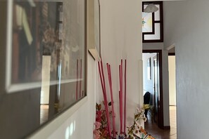A hallway with a mirror reflecting a room, a vase with flowers, and a door leading to another room.