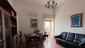 A living room with a black leather sofa, a dining table with chairs, a chandelier, and a television set. - All' Arco - Elegant apartment in the historic center of Fuscaldo (Fuscaldo)