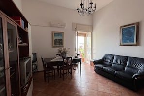 A living room with a black leather sofa, a dining table with chairs, a chandelier, and a television set. - All' Arco - Elegant apartment in the historic center of Fuscaldo (Fuscaldo)