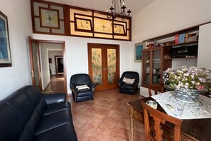 Ein Wohnzimmer mit einer Couch, zwei Sesseln, einem Holztisch und einer Kommode mit Büchern und Dekoration.