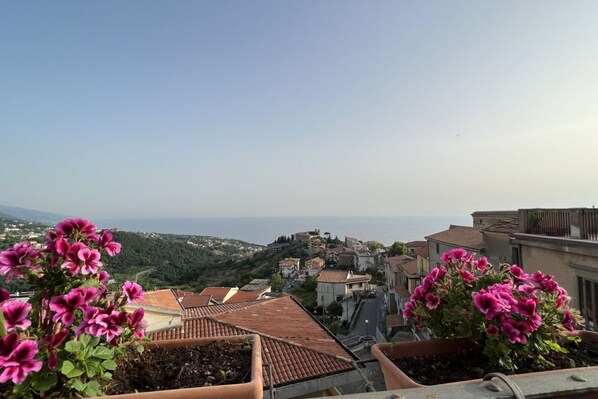A terrace with potted pink flowers, a view of a hillside town, and terracotta rooftops. - All' Arco - Elegant apartment in the historic center of Fuscaldo (Fuscaldo)