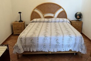Una cama con una colcha estampada con flores, dos mesitas de noche con lámparas y un globo terráqueo sobre una de ellas.