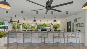 Un espace bar doté d’un ventilateur de plafond, de plusieurs luminaires suspendus et offrant une vue sur la piscine extérieure.