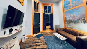 A modern living room with a large TV, a ceiling fan, a sofa, and a large window with a cityscape view. - The Ruby Peak Condo is part of the historic Litch Hotel (Enterprise)