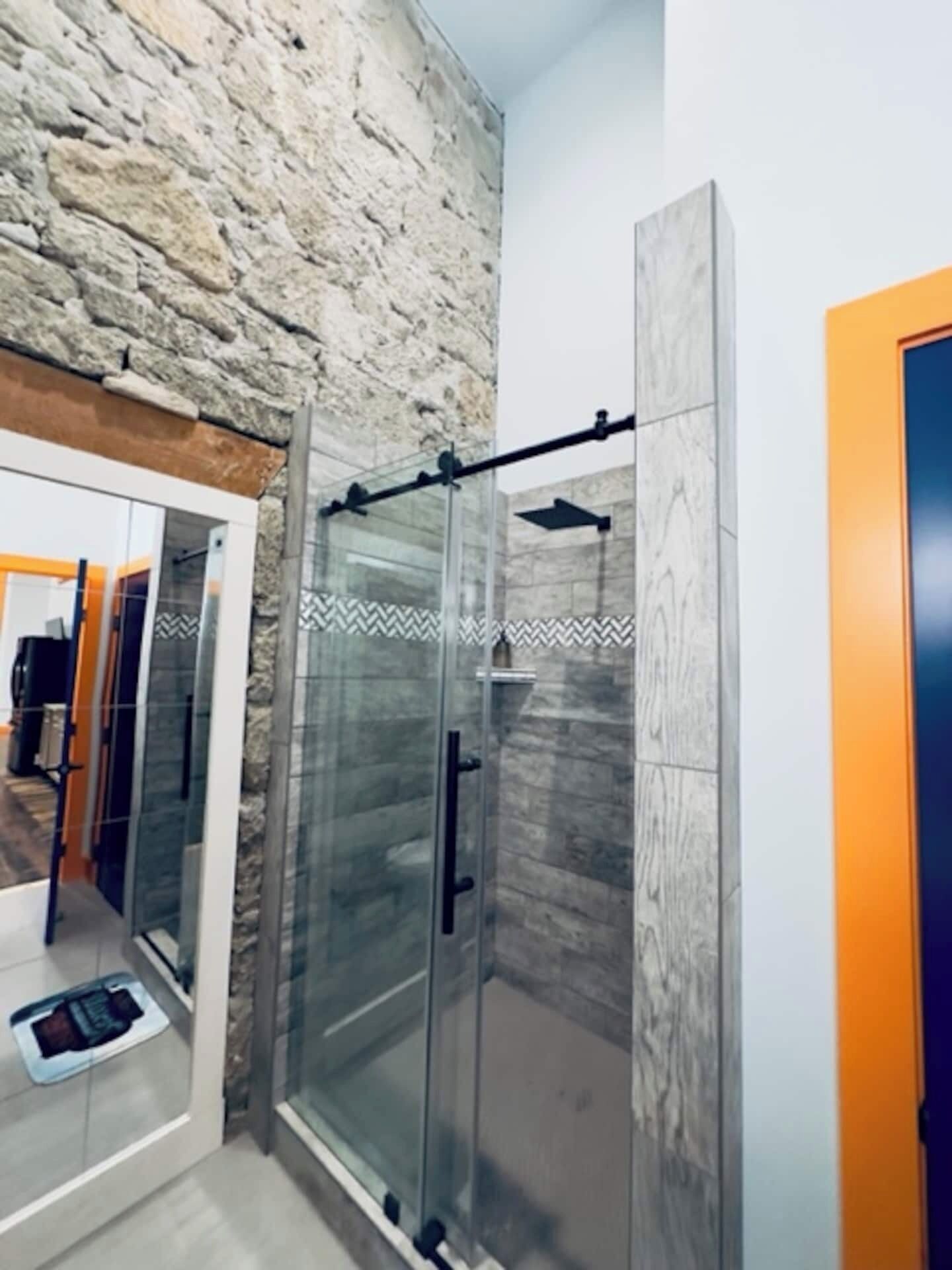 Une salle de bain moderne avec une douche à parois de verre, un mur en pierre et un meuble-vasque apparent.