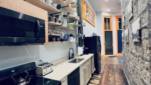 A modern kitchen with wooden shelves, a black stove, and a stone wall. - The Ruby Peak Condo is part of the historic Litch Hotel (Enterprise)