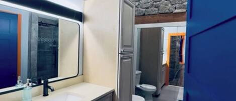 A modern bathroom with a stone accent wall, a large mirror, and a built-in toilet.