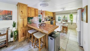 Une cuisine avec des meubles de rangement en bois, un îlot central en marbre, des tabourets de bar, un réfrigérateur et un évier.