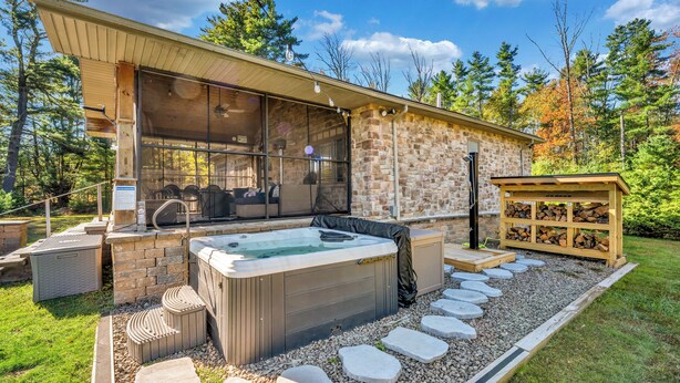Un espace moderne aménagé à l’extérieur avec un jacuzzi, des murs en pierre, une terrasse en bois et un foyer en pierre.