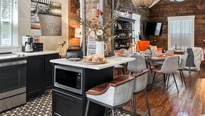 Una cocina moderna con una isla central, un comedor con techos altos y paredes de ladrillo visto, y una zona de estar acogedora.