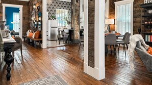 Amplia sala de estar con piso de madera, comedor con sillas modernas y cocina con refrigerador y salpicadero.