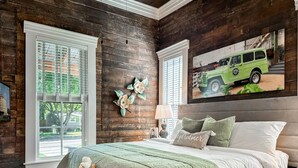 Un dormitorio con pared de madera, un cuadro de un vehículo verde y una cama con colcha verde.