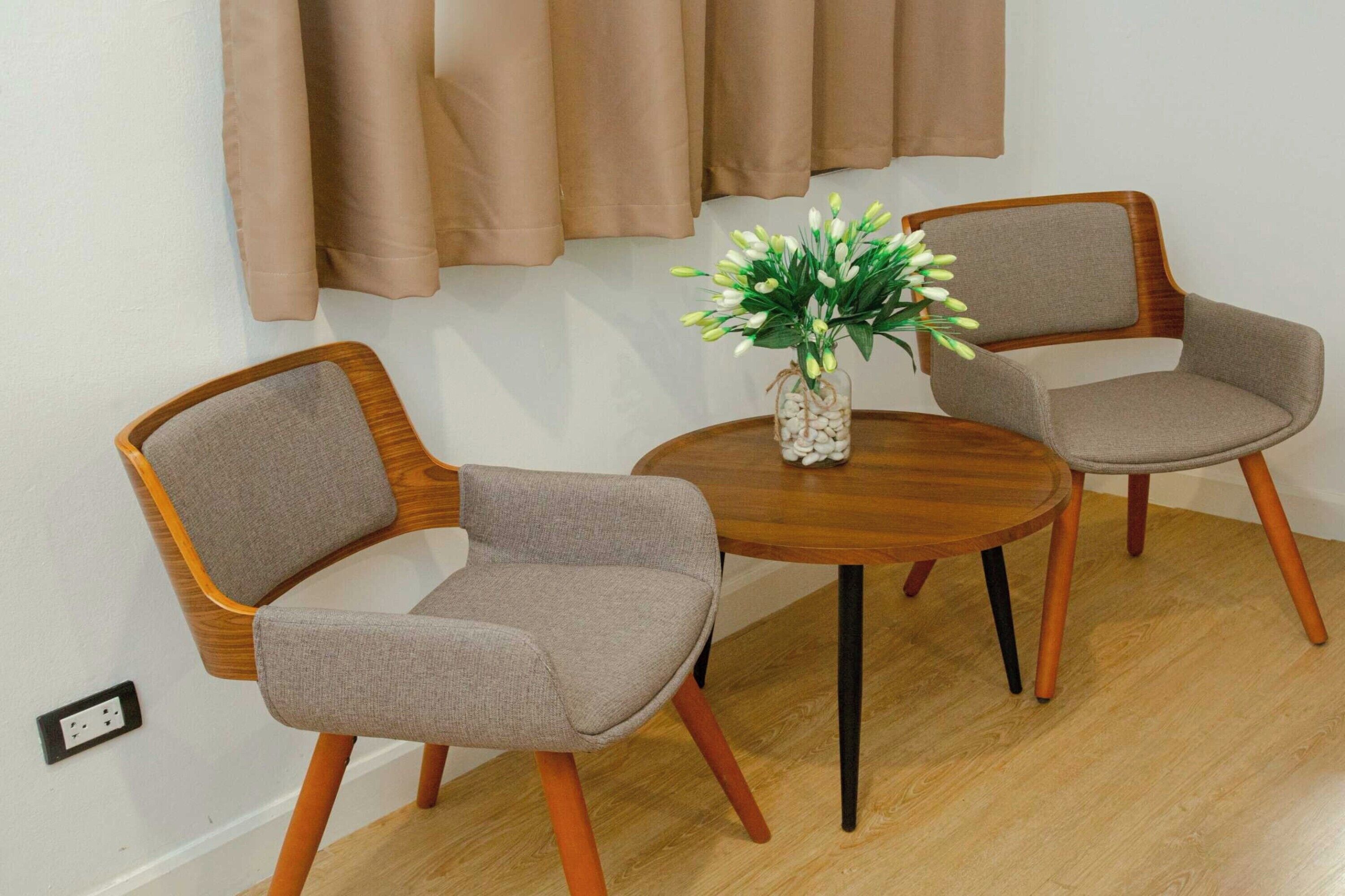 A dining area with two chairs and a table, a vase with flowers, and a wall with curtains.