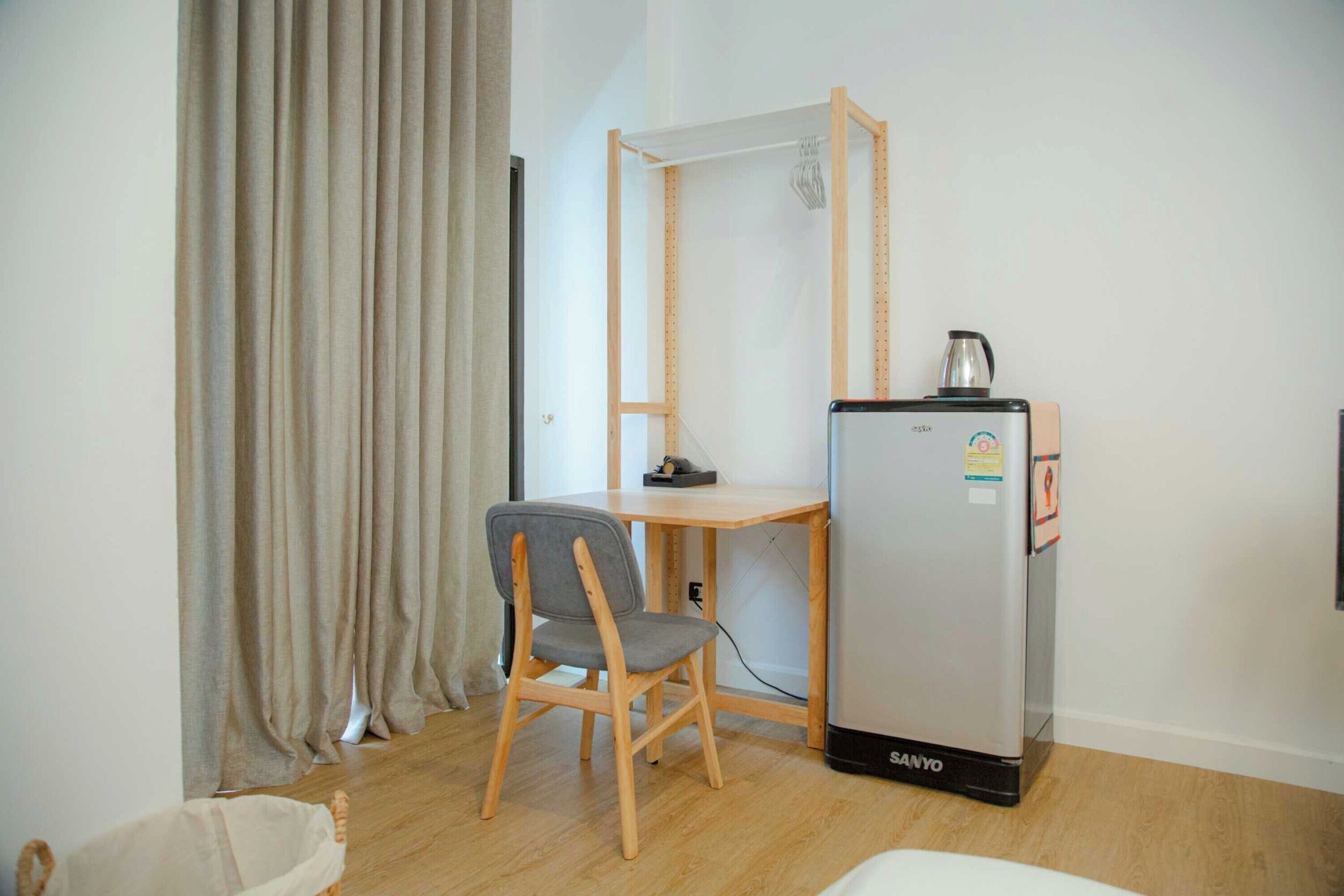 A compact room with a wooden desk, a chair, a refrigerator, and a curtain.