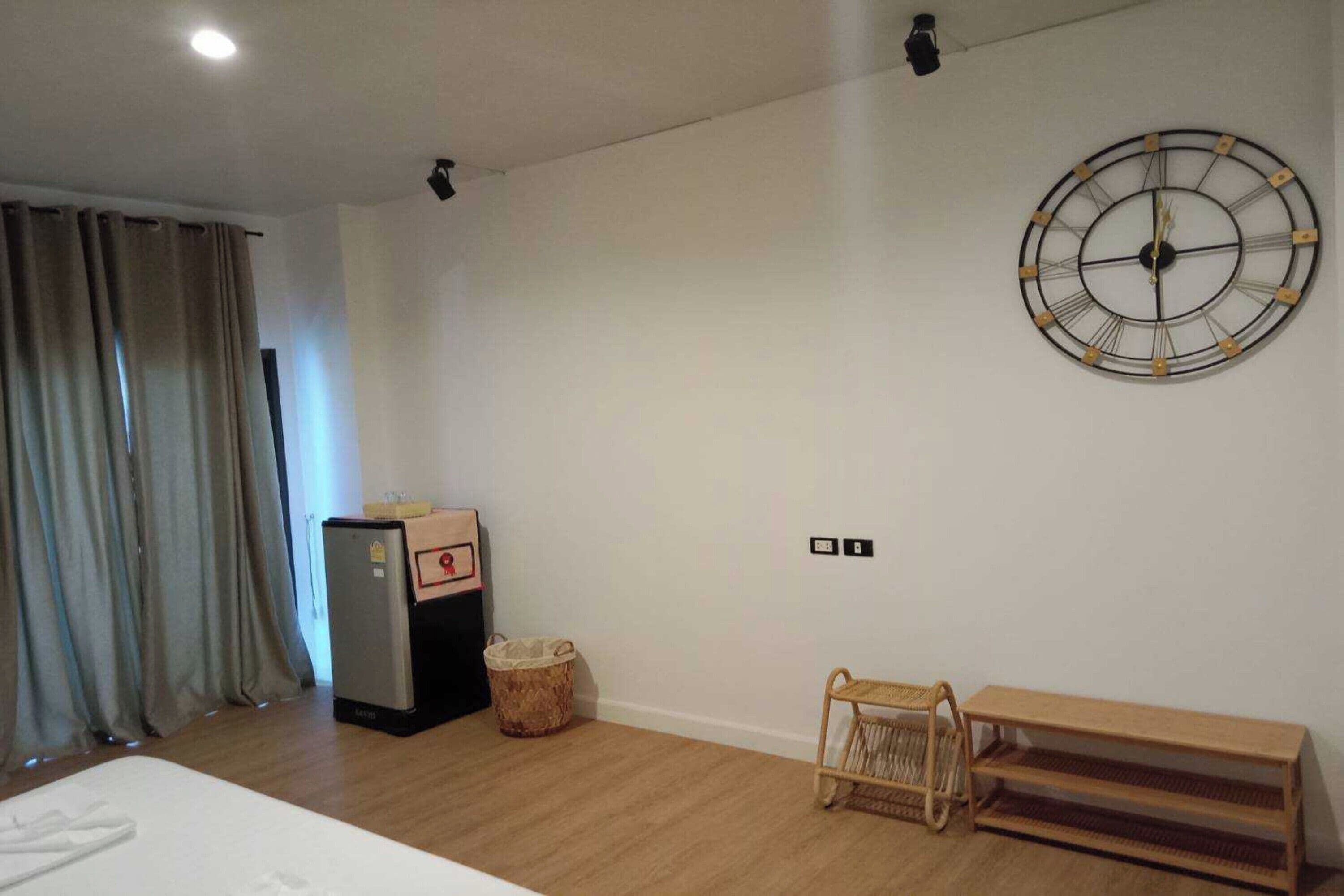 Ein Hotelzimmer mit Bett, Wanduhr, Minibar, Mülleimer und einer Bank.