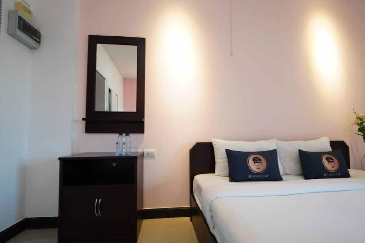 Hotellihuone, jossa on sänky, lipasto, peili ja seinään kiinnitetyt valaisimet.